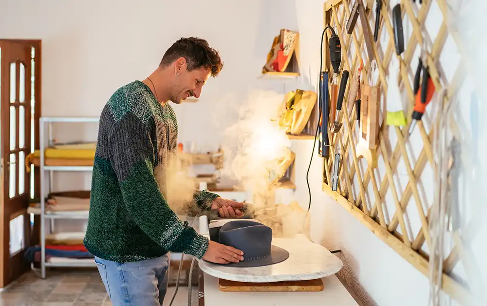 Man using a hat steamer to shape a hat.