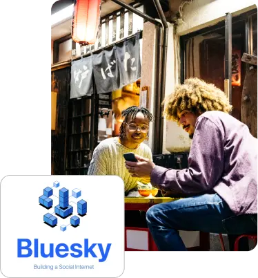 Man and woman looking at phone with inset of Bluesky logo and blue building blocks